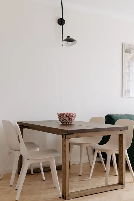 Jadalnia w stylu minimalistycznym z drewnianym stołem, jasnymi krzesłami i nowoczesnym oświetleniem.