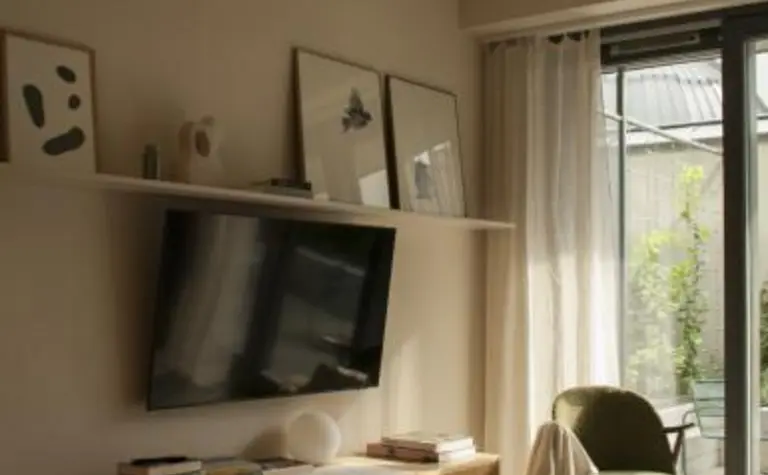 Wnętrze salonu w stylu eklektycznym z telewizorem, komodą i dużymi oknami.