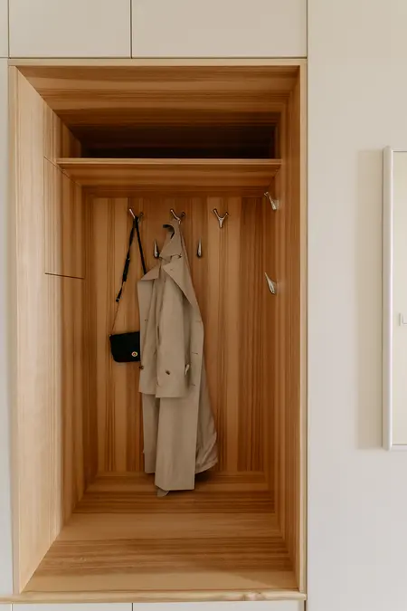 Minimalistyczna garderoba z drewnianym wnętrzem, wieszakami i płaszczem.