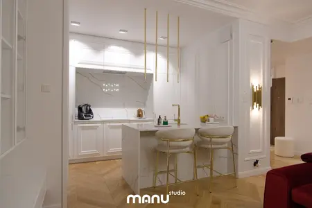 Nowoczesna kuchnia z białymi meblami, złotymi detalami oraz marmurowym blatem.