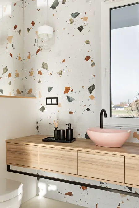 Nowoczesna łazienka z elementami art deco, boho i glamour, z drewnianą szafką i różową umywalką.