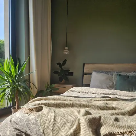 Sypialnia boho z zieloną ścianą, roślinami i drewnianym łóżkiem.