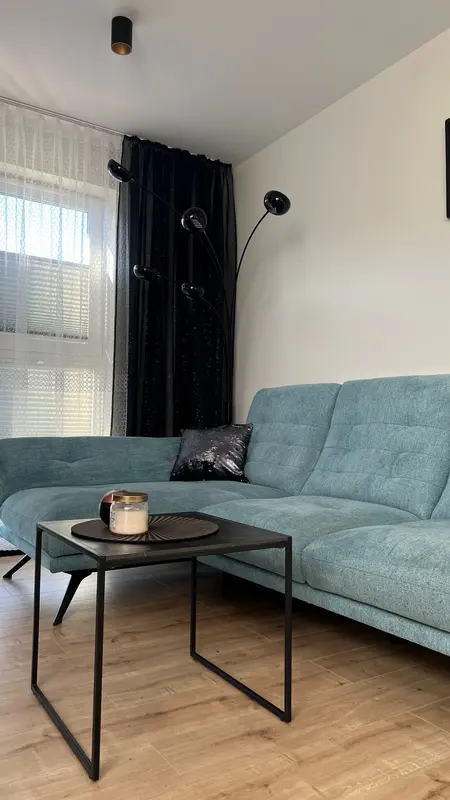 Wnętrze salonu w stylu nowoczesnym z niebieską sofą, czarnymi zasłonami i drewnianą podłogą.