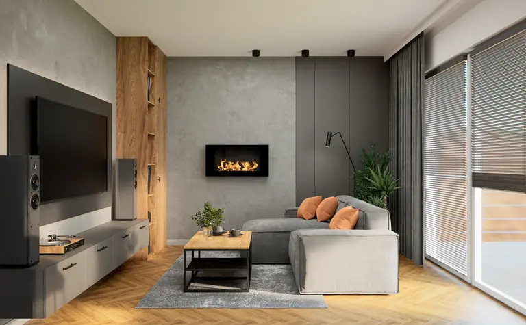 Stylowy salon z szarą sofą, pomarańczowymi poduszkami i ściennym kominkiem. Wnętrze uzupełnia duży telewizor, drewniane akcenty i stolik kawowy, tworząc elegancki i przytulny wystrój.