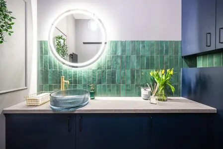 Wnętrze łazienki z zielonymi kafelkami, umywalką i lustrami w stylu industrialnym i współczesnym.