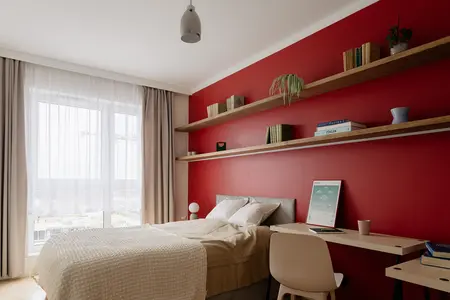 Sypialnia w stylu minimalistycznym z czerwoną ścianą, drewnianymi półkami i nowoczesnym biurkiem.