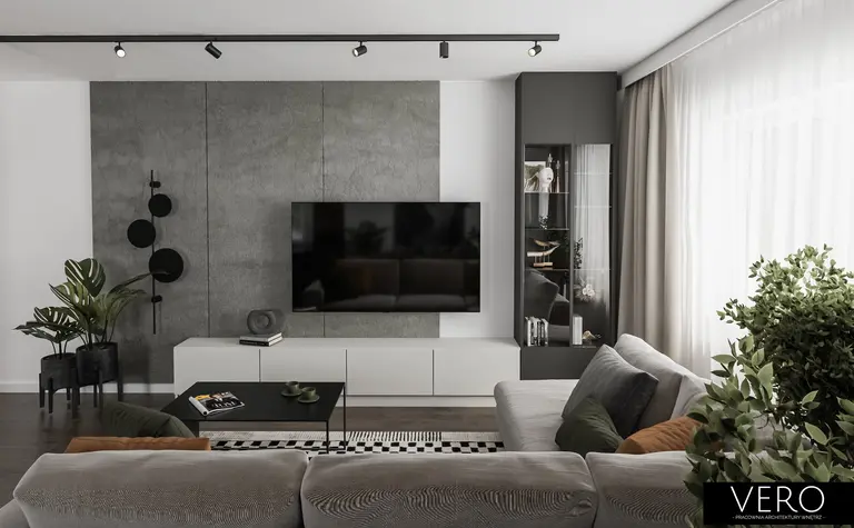 Minimalistyczny salon z zielonymi roślinami i szarymi meblami.
