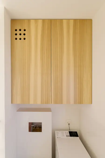 Minimalistyczna pralnia z drewnianymi szafkami i nowoczesnym sprzętem AGD.