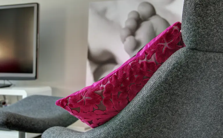 Wnętrze salonu z szarym fotelem i różową poduszką, minimalistyczny styl.
