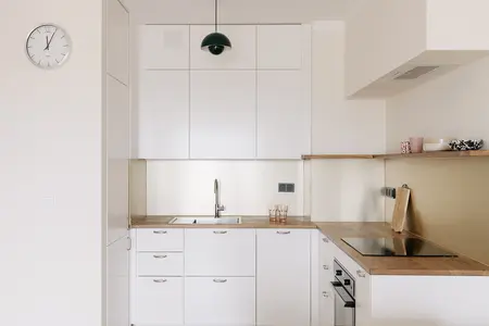 Kuchnia w stylu minimalistycznym z białymi meblami i drewnianym akcentem.