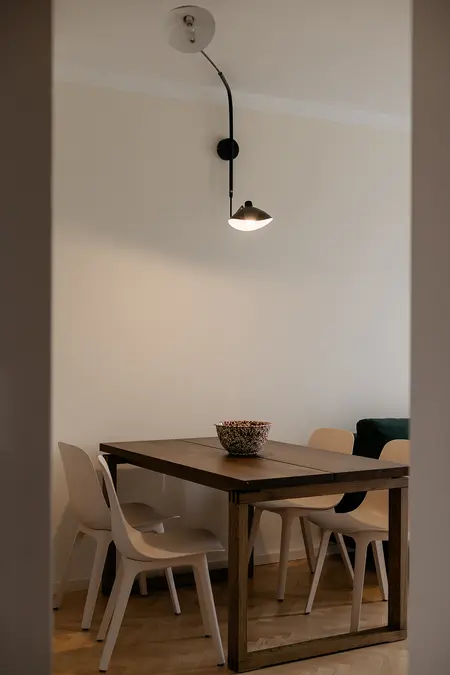 Jadalnia w stylu minimalistycznym z drewnianym stołem, jasnymi krzesłami i nowoczesnym oświetleniem.