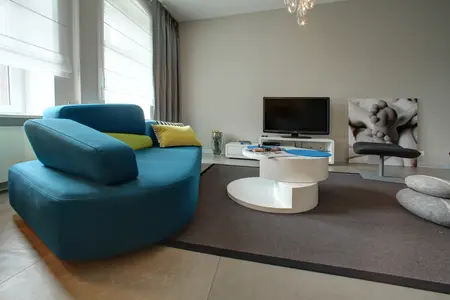 Wnętrze salonu z niebieską sofą, białym stolikiem i minimalistycznym wystrojem.