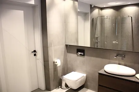 Nowoczesna łazienka z minimalistycznym designem, szarymi płytkami i białą umywalką.