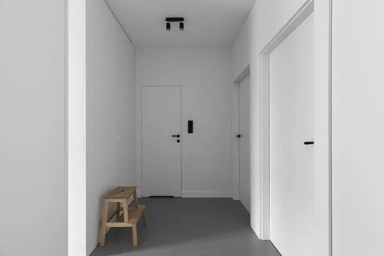 Przedpokój z minimalistycznym wystrojem, białe ściany i drewniana ławka.