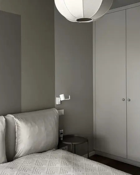 Sypialnia w stylu minimalistycznym z szarymi ścianami, białymi meblami i lampą.