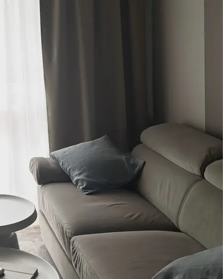 Wnętrze salonu w stylu minimalistycznym z szarym narożnikiem i białymi zasłonami.