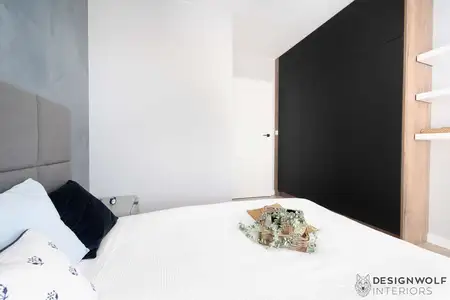 Wnętrze sypialni z szarym tłem, czarną szafą i białą pościelą. Styl industrialny.
